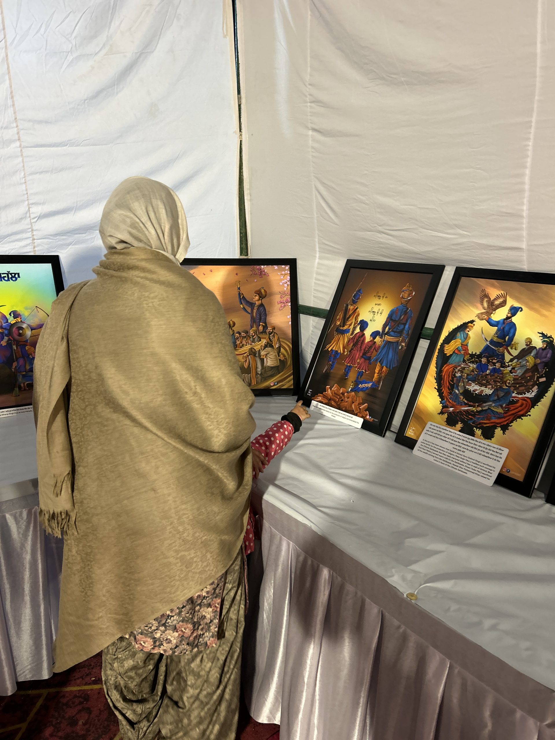 An elder before a row of framed Sikh history artworks