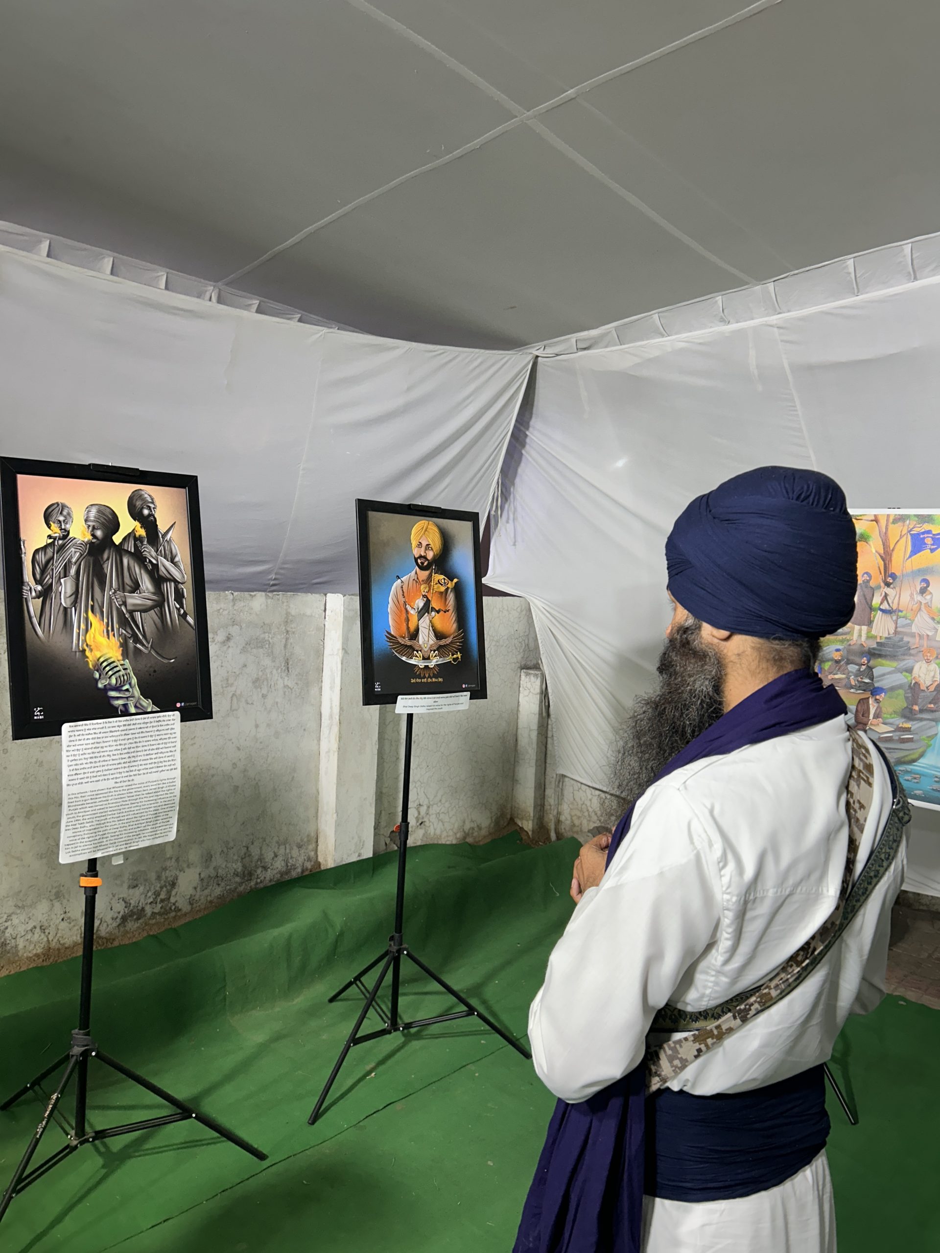 A visitor between two framed artworks at a Sikh art exhibition